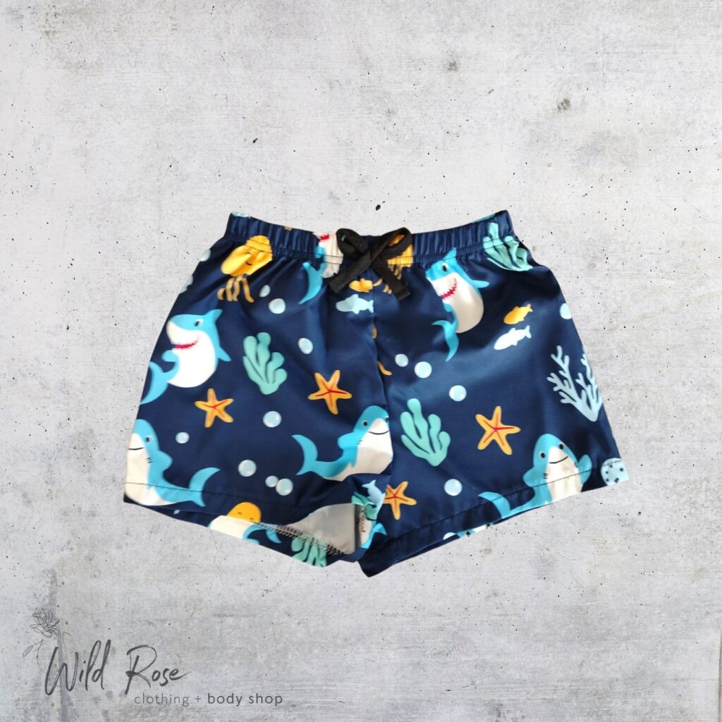 Deep Sea Sharks Swim Shorts featuring colourful sharks, whales, starfish and sea creatures on a navy blue background, perfect for kids' swimming and beach days.
