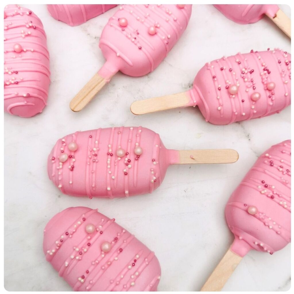 Yummy Treats LolliCake pink cake pops on sticks decorated with drizzled icing and sprinkles, perfect for parties and dessert tables.